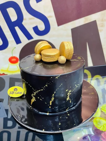 A sophisticated 1.5kg black marble cake with gold splatter, topped with elegant golden macarons.