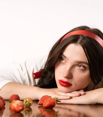A creative portrait with a strawberry theme. The model's wistful expression and the vibrant red props create a dreamy, almost surreal atmosphere.