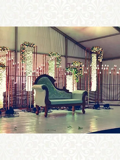 A vintage-inspired stage with a classic chaise lounge. The backdrop is made of modern metal frames with floral pillars and candle-like lights, blending old-world charm with contemporary design.