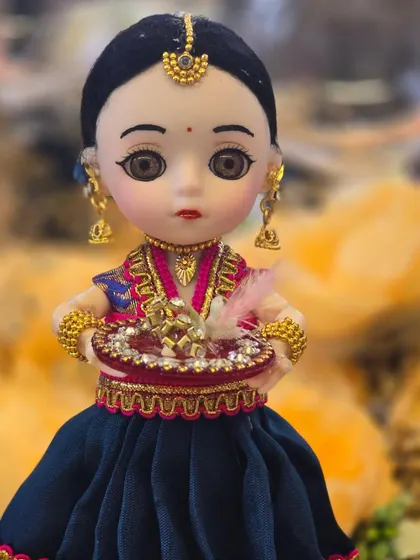 A close-up of a custom-made doll, showing the intricate details of her lehenga, jewelry, and the small 'aarti thali' she is holding.