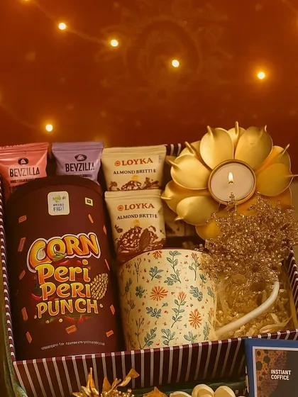 The "Roshni Ka Tohfa" (Gift of Light) is perfect for Diwali. This hamper includes a printed coffee mug, a lotus-shaped brass diya, peri peri corn snacks, and almond brittle.