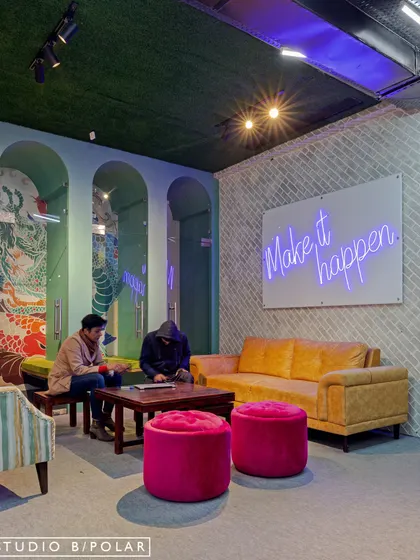The 'Make it happen' neon sign reinforces the motivational theme of this coworking space. Paired with comfortable seating and soft lighting, this corner becomes a perfect spot for brainstorming and focused work.