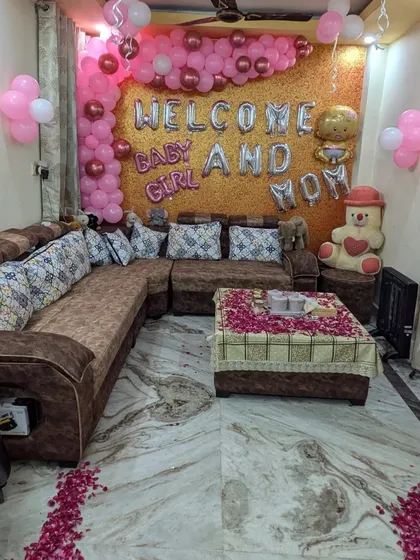 A wider view of the 'Welcome Baby and Mom' decor, showing the balloon arrangement, decorated coffee table, and rose petal path on the floor.