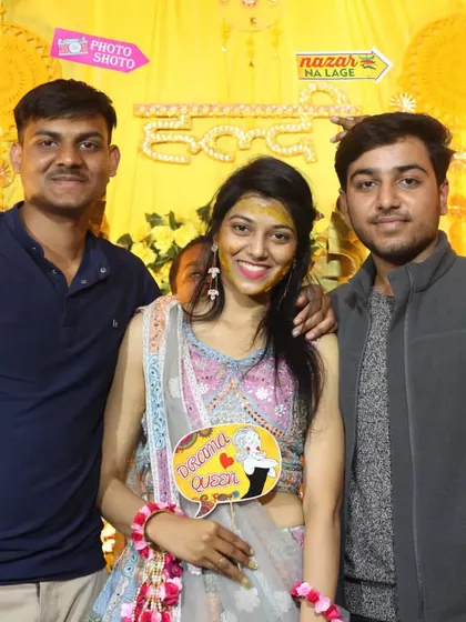 Group photos can be fun too. Here, the bride-to-be poses with friends and quirky props like 'Drama Queen' and 'Nazar Na Lage' signs, adding a modern twist to the traditional Haldi celebration.