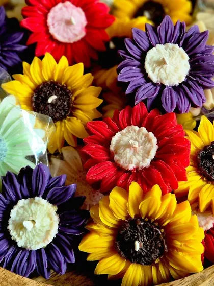 A bowl of my colorful floating sunflower candles. I offer them in a variety of vibrant shades like yellow, red, and purple to brighten up your festive decor.