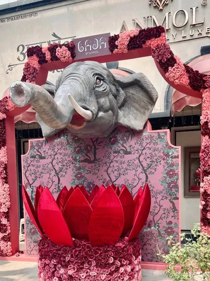 A majestic entrance created for luxury brand Anmol Jewellers. A large, sculpted elephant head emerges from a custom backdrop, framed by an arch of pink and crimson florals, making a powerful and artistic statement for the brand's event.
