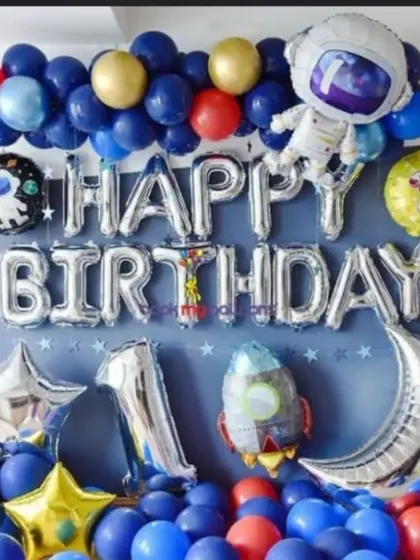 A classic 'Happy Birthday' balloon wall with a space theme, using silver foil letters and astronaut and planet balloons.