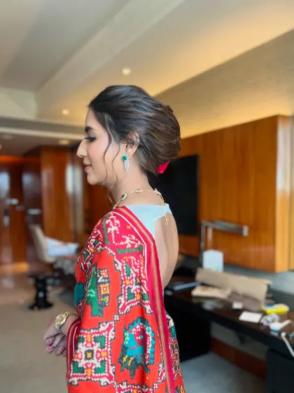 A side profile of the red rose bun, showing its sleekness and how it pairs with a modern, backless blouse.