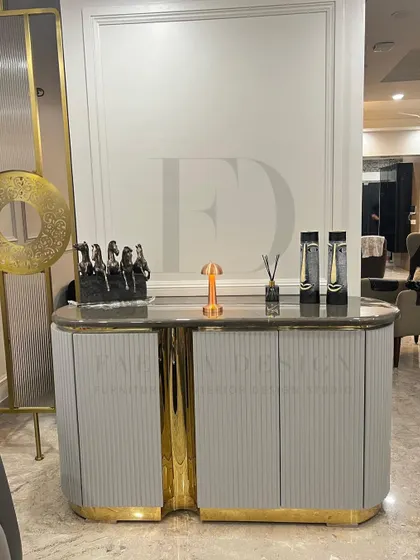 A stunning console table designed for a foyer. It features a grey fluted body, a dark marble top, and a central accent of polished gold-toned metal, creating a luxurious first impression.