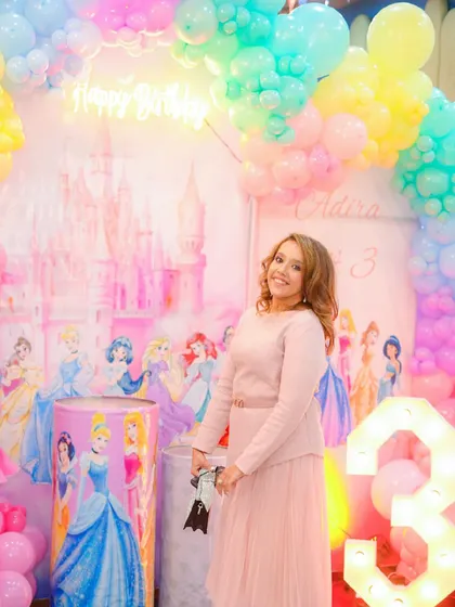 A guest poses in front of the pastel-colored princess castle backdrop, complete with a light-up number 3.