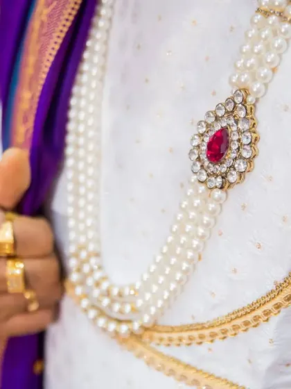 A detail shot of the groom's pearl necklace and the elegant brooch, highlighting the fine craftsmanship of his wedding attire.