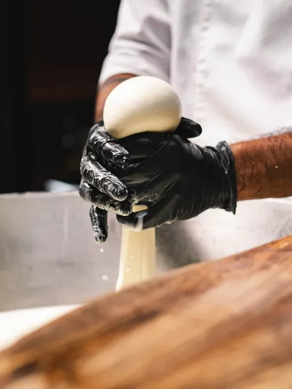 A ball of fresh mozzarella is pinched off from the larger mass. Each ball is shaped by hand, ensuring uniformity in size and a perfect, smooth surface.