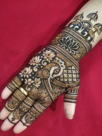A bold and striking design with a large peacock and lotus motifs. The use of negative space and thick lines makes the design stand out, while the 'jhumka' motifs on the wrist add a festive touch.