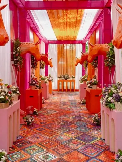 Haldi, but make it equestrian chic. This bold entranceway combines vibrant pinks and oranges with floral-adorned horse sculptures to create a whimsical and unforgettable welcome for a fun-filled celebration.