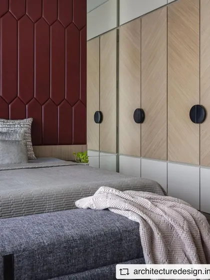 Another view of the bedroom in 'Aria Residence', showcasing the custom wardrobes with a chevron veneer pattern and a bold, geometric red upholstered headboard.