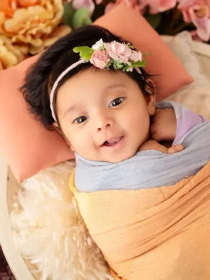 A happy one-month-old baby, swaddled snugly and surrounded by a wreath of colorful flowers.