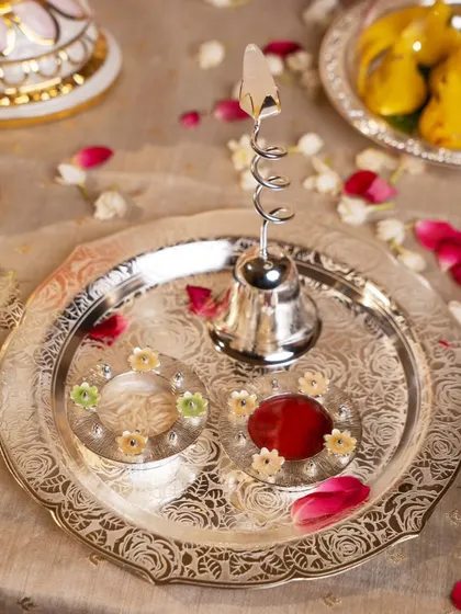 A sacred pooja thali, crafted in silver with intricate floral etching. This piece, complete with a bell and containers for roli and rice, makes divine rituals feel even more special with its elegance and detail.