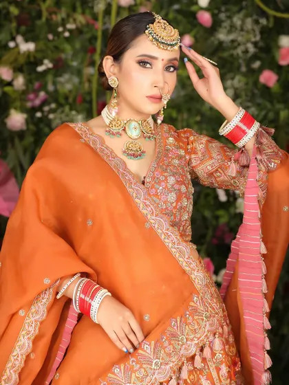 A stunning bridal portrait featuring a model in a bright orange lehenga against a floral wall, perfect for spring or summer collections.