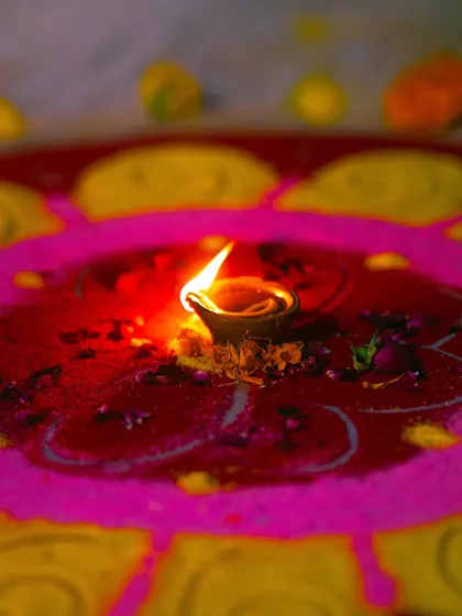 A single diya placed in the center of a colorful rangoli. The vibrant colors and the gentle flame create a beautiful and traditional Diwali image.