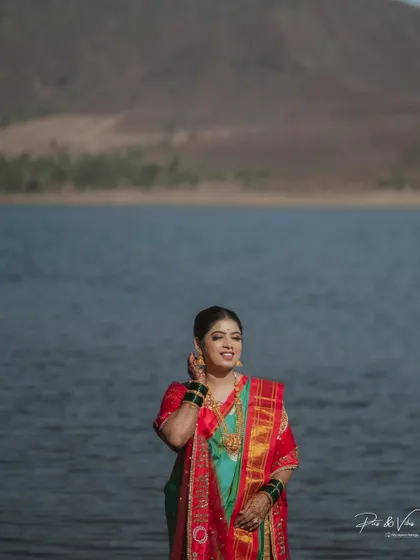 The bride adjusts her earring, her smile radiant, as she stands by the tranquil lakeside, a perfect blend of elegance and nature.