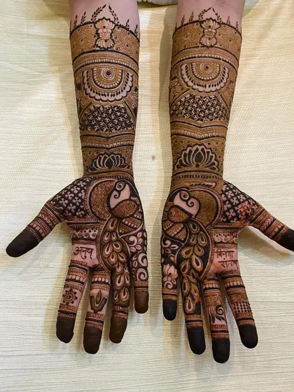 The complete bridal look, with matching peacock designs on both palms and intricate patterns covering the forearms. The bride's and groom's names are hidden within the art.