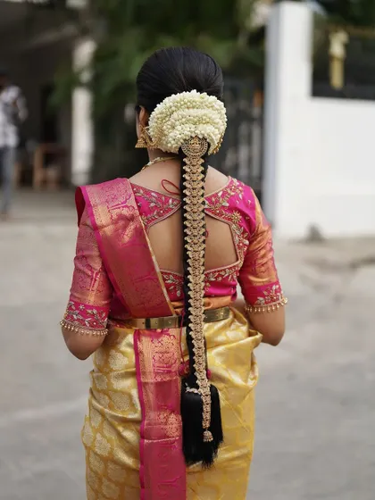 A South Indian bridal look is incomplete without a stunning hairstyle. Here, I've created a traditional long braid, intricately decorated with fresh jasmine flowers and a beautiful golden jadai, perfectly complementing her silk saree.