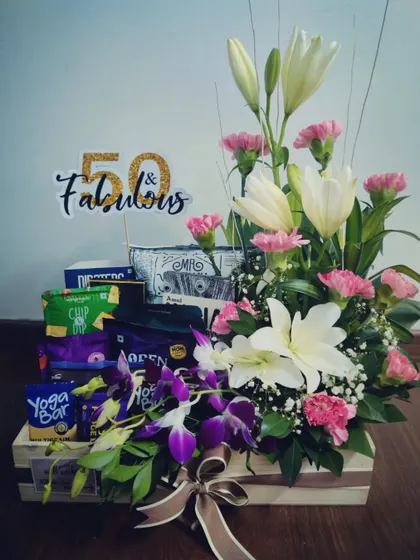 This 50th-anniversary hamper is a masterpiece of fresh flowers. It combines white lilies, pink carnations, and purple orchids with a selection of healthy snacks for a truly sophisticated gift.