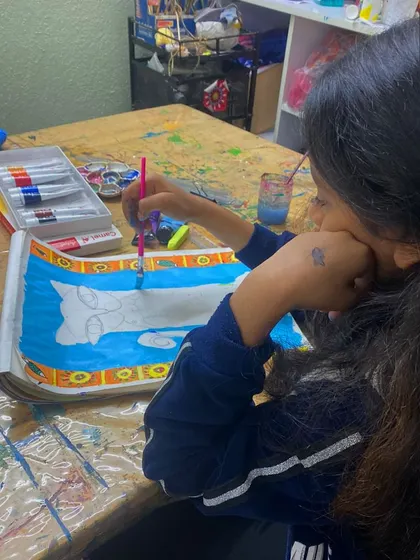 A young girl is completely absorbed in her Madhubani-style painting, carefully filling in the intricate patterns.