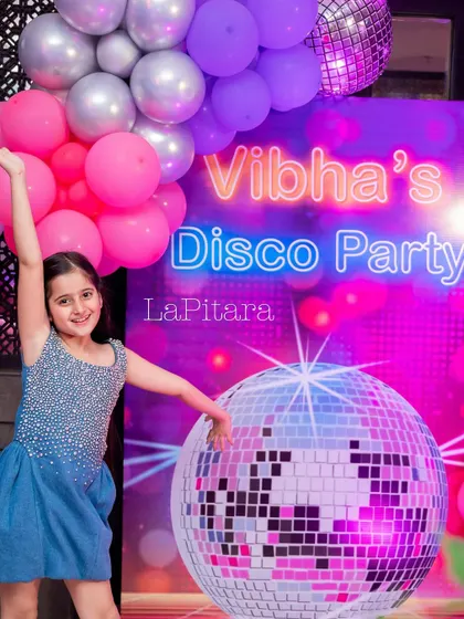 The birthday girl posing with a giant disco ball prop, capturing the fun and spirit of her party.