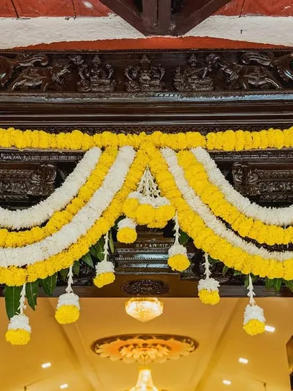 A close-up of a traditional floral 'thoranam' made of marigold and jasmine, adorning a beautifully carved wooden doorway.