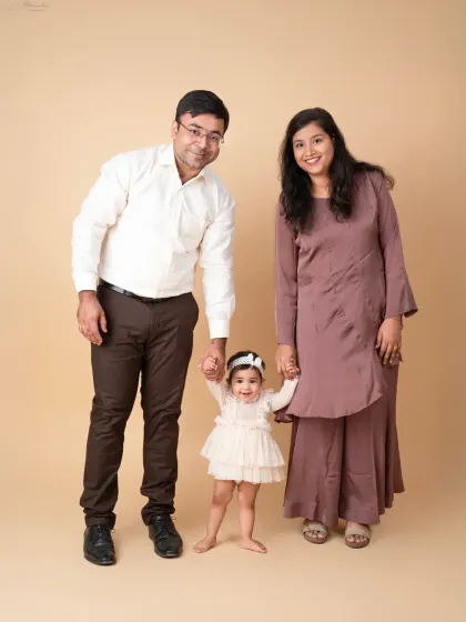 A fun and loving family portrait, with mom and dad holding their daughter's hands as she takes a step.