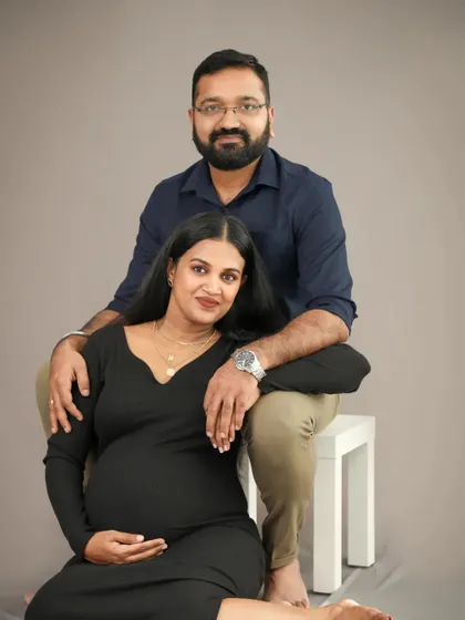 A gorgeous and classic studio portrait of an expecting couple. They are posed elegantly, looking directly at the camera with warm smiles, capturing their unity.