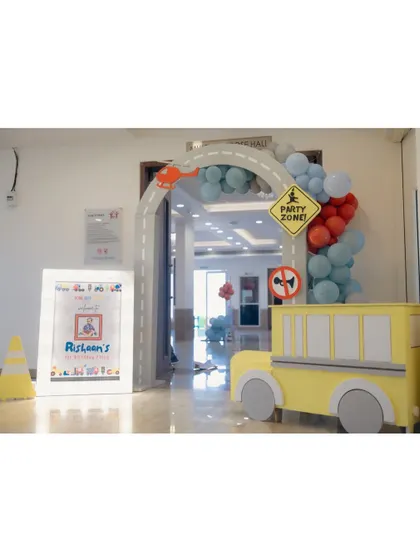An indoor entrance for a transportation party, with a road arch, a 'Party Zone' sign, and a cute yellow bus prop to welcome the little guests.