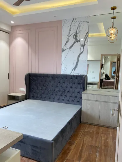 The completed bedroom view, now with finished flooring and a custom wardrobe. The combination of a grey velvet bed, pink wall panels, and marble creates a look of modern luxury.
