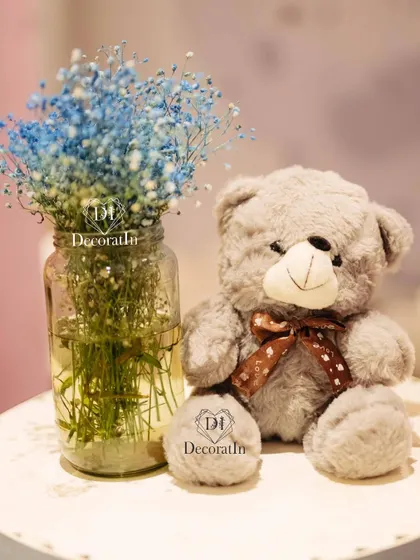 A simple and sweet detail: a grey teddy bear next to a vase of blue baby's breath.