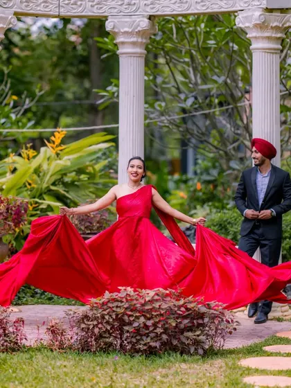A candid moment of movement and grace. The bride-to-be walks through the garden, her red gown flowing behind her, creating a beautiful and natural portrait.