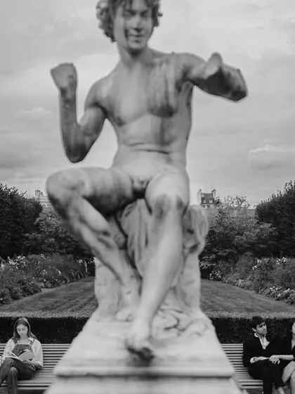 A quirky and candid moment captured in Paris, where the couple sits on a bench beneath a statue, creating a humorous and memorable scene.