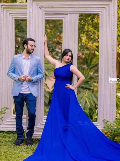 Using the giant picture frames as a creative prop. The couple strikes a stylish, editorial pose, with the flowing blue gown adding a splash of color and drama to the scene.