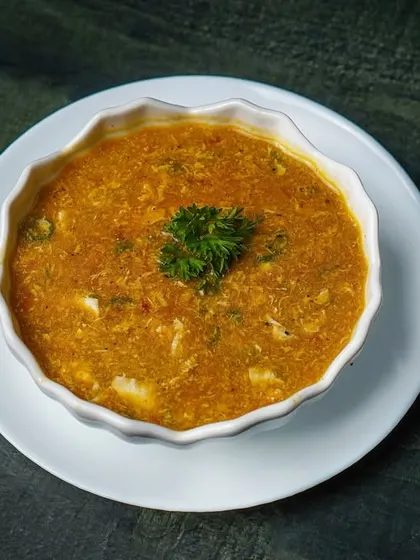 A bowl of creamy sweet corn soup, presented simply in a white bowl on a dark surface. The moody lighting adds depth and texture to the shot.