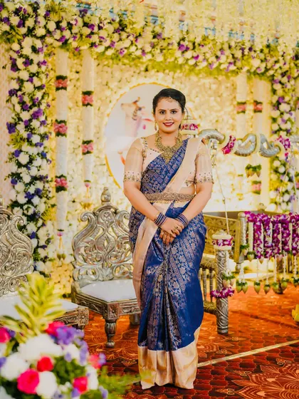 The client posing against a grand floral backdrop, her custom blouse perfectly complementing the rich blue and gold of her saree.