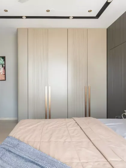 This elegantly curated bedroom exemplifies modern luxury with a seamless blend of muted neutrals and warm earthy tones. The design concept revolves around minimalist sophistication, featuring sleek, floor-to-ceiling wardrobes with subtle metallic accents.