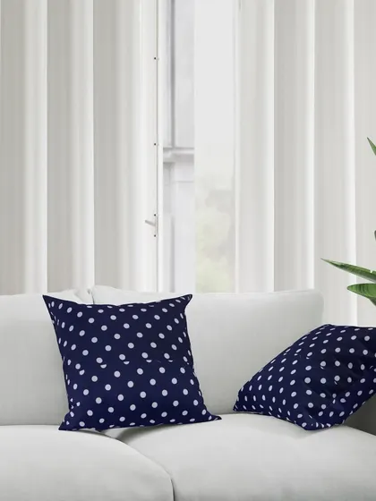 Two navy polka dot cushions placed on a modern white sofa. This demonstrates how the product can be used to add a pop of color and pattern to a living room.