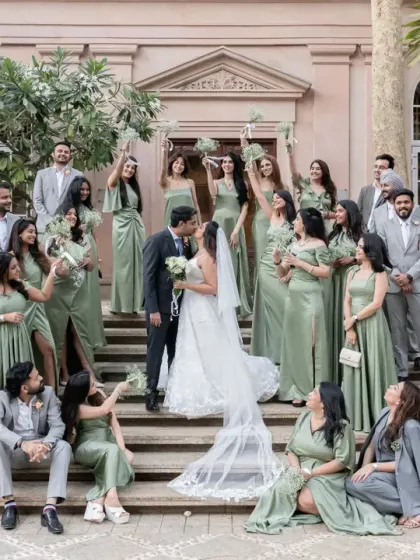 A picture-perfect moment with the entire bridal party on the steps of the venue. The coordinated outfits and the couple's central kiss create a stunning and memorable group portrait.