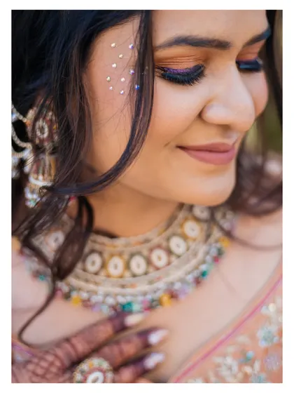 A close-up of the bride's stunning makeup for the Haldi function, featuring a pop of blue eyeliner and delicate face gems that add a touch of modern glam.