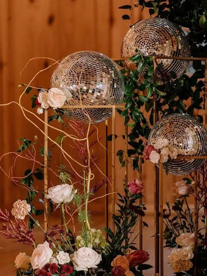 A stylish decor detail for a modern cocktail party. Disco balls are placed on golden stands and accented with pink roses for a chic, glamorous look.