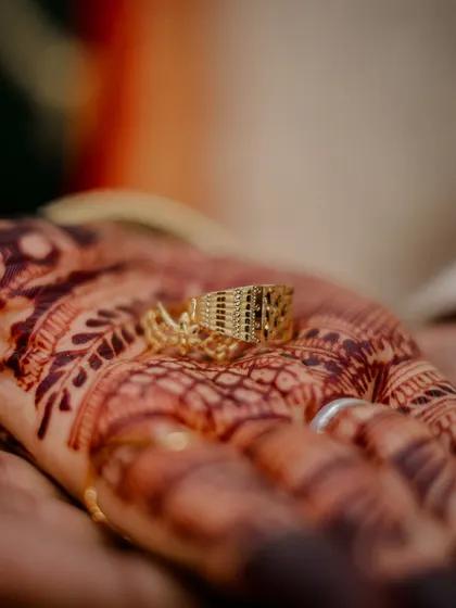 A detailed shot of the groom's engagement ring resting on the bride's henna-covered palm.