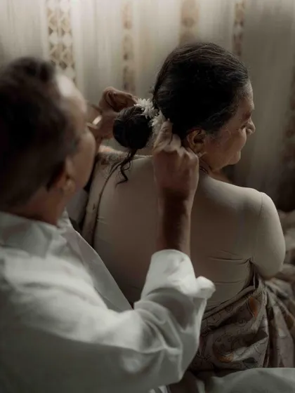 A close up of a loving gesture. The act of him helping her with her hair is a small detail that speaks volumes about their partnership and care for one another.