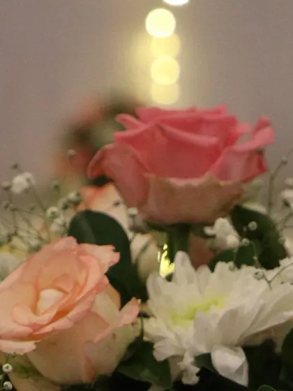 A close-up of a delicate floral arrangement with soft pink roses and baby's breath. The bokeh effect from the background lights adds a touch of magic.