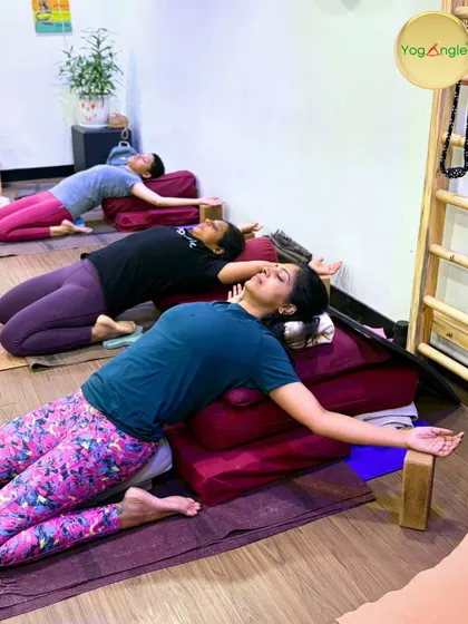 Students in a workshop find deep relaxation in a supported Supta Virasana. Using bolsters for back support allows them to release tension in their quadriceps and hip flexors while focusing on calm, even breathing.