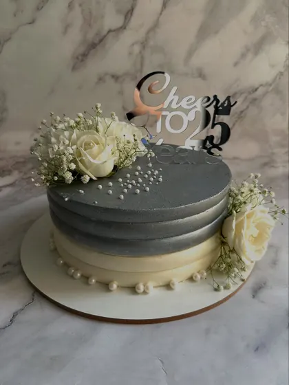 A chic and elegant cake for a 25th silver anniversary. The design features a silver-to-white ombre effect, adorned with fresh white roses, baby's breath, and delicate sugar pearls.